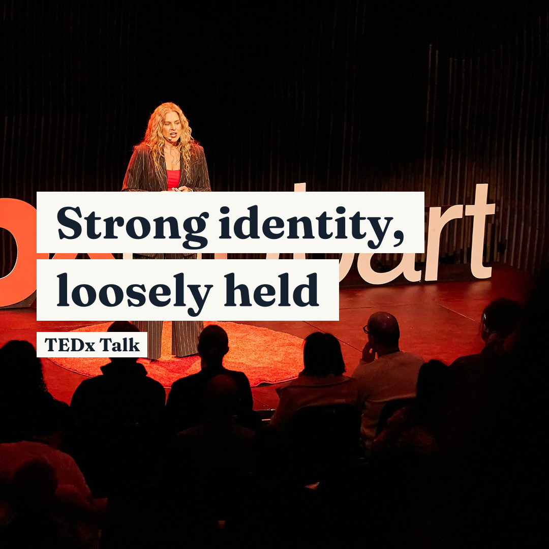 A woman gives a presentation on stage before an audience, with text reading, 'Strong identity, loosely held TEDx Talk'.